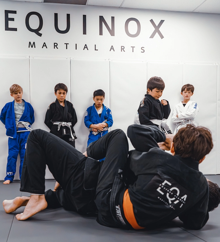 Equinox's student leader demonstrating a Brazilian Jiu-Jitsu technique on Adam, instructor at Equinox Academy, for the kids and teens' gi BJJ class.
