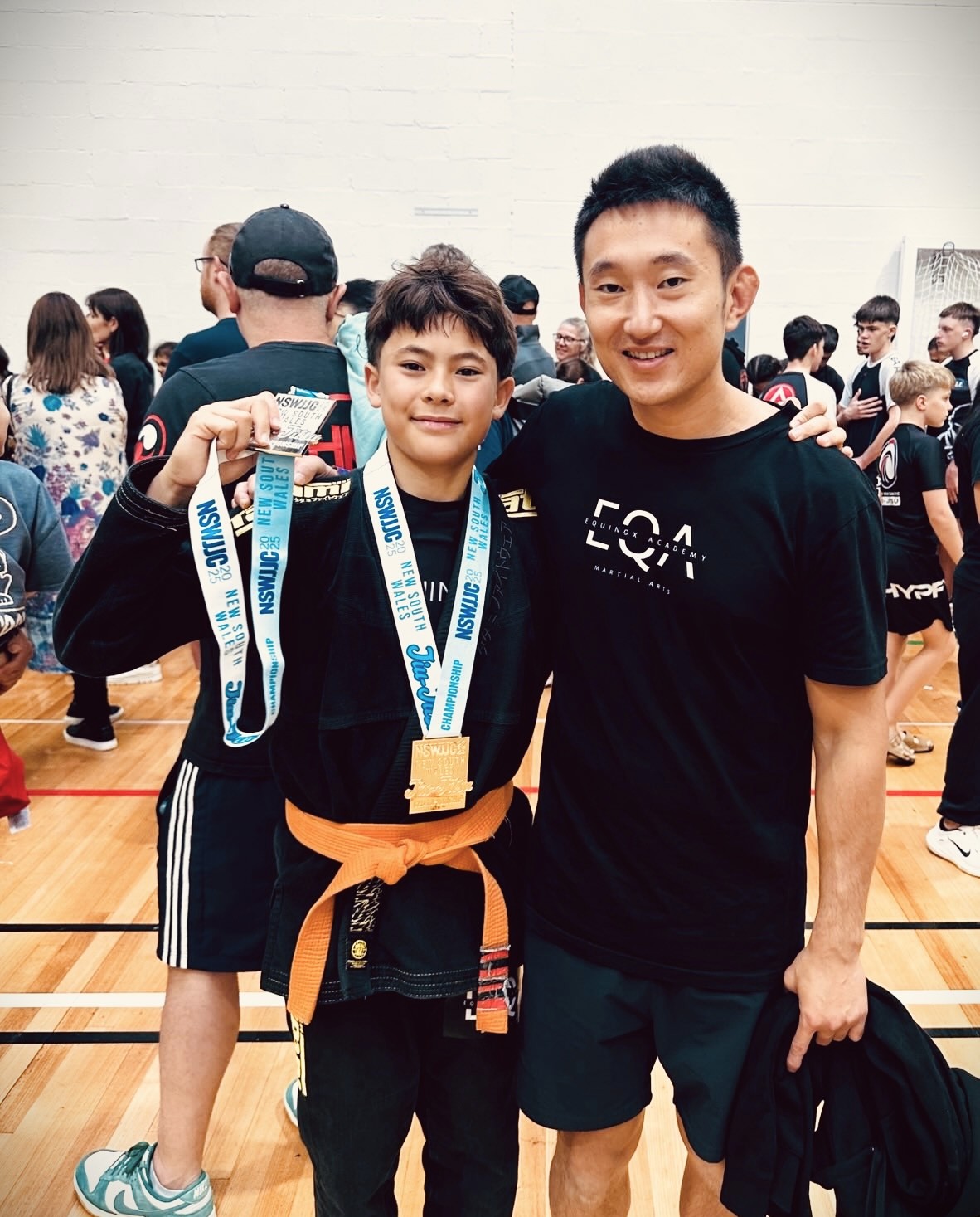Teenage student winning a medal at a Brazilian Jiu-Jitsu (BJJ) competition, standing together with Equinox Academy coach, James